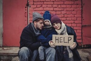 Poor,Young,Family,With,Help,Sign,On,Dirty,Street