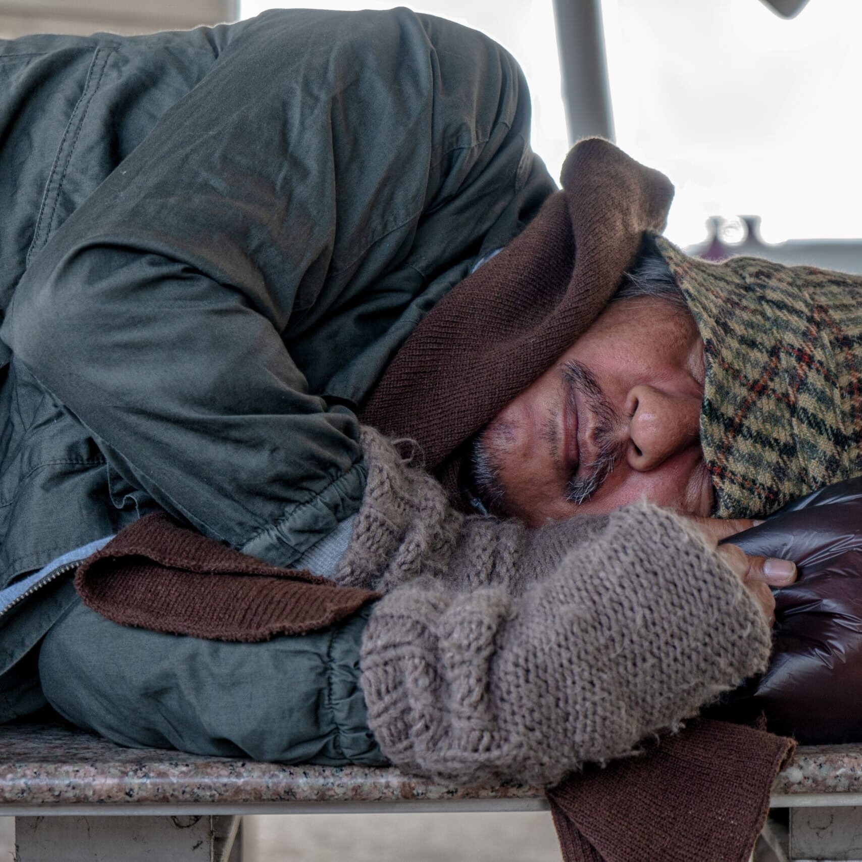 Homeless,Male,Sleeping,On,Stone,Bench,At,Train,Terminal