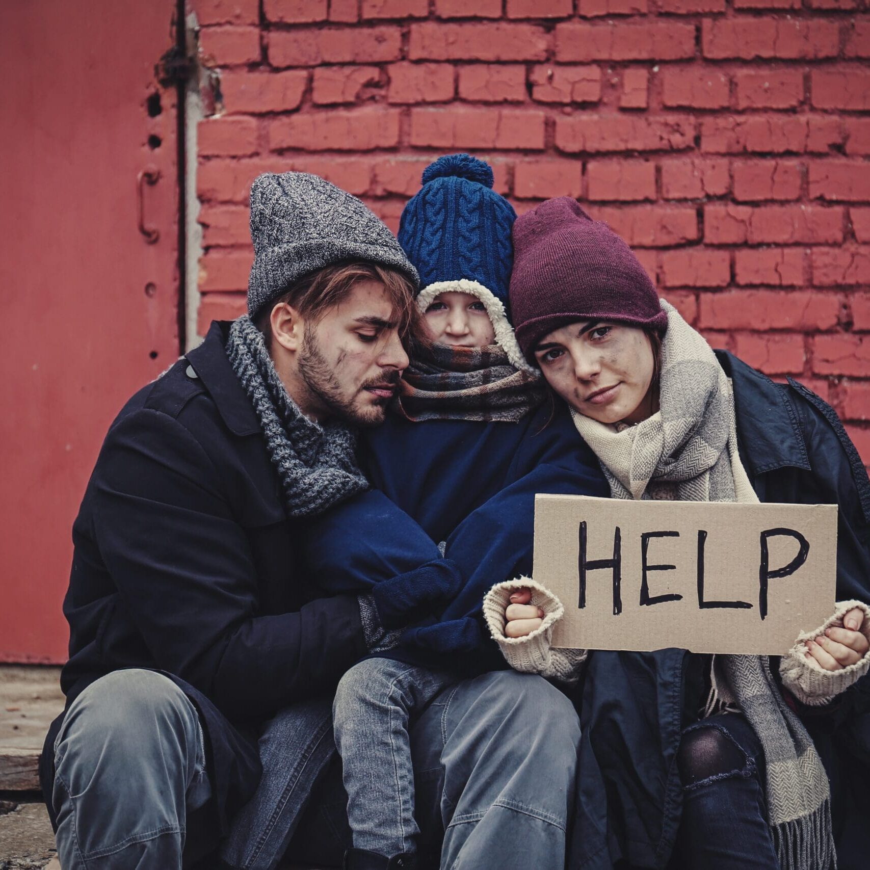 Poor,Young,Family,With,Help,Sign,On,Dirty,Street